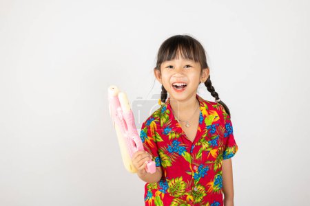 Photo for Happy Songkran Day, Asian kid girl with floral shirt hold water gun, Thai child funny hold toy water pistol and smile, isolated on white background, Thailand Songkran festival national culture concept - Royalty Free Image