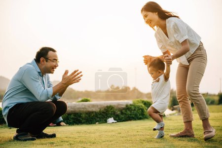Téléchargez les photos : Portrait d'une famille aimante passant du temps de qualité dans la nature, apprenant à leur petite fille à marcher par une belle journée de printemps. concept de soutien aux parents d'enfants - en image libre de droit