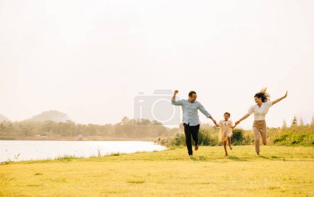 Photo for A group of family father, mother and child running and playing in a beautiful nature setting, with green grass and a sunny sky, feeling free and happy, Happy Family Day Concept - Royalty Free Image