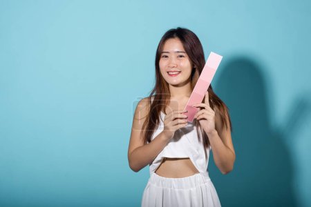 Photo for Asian beautiful young woman holding skin color scale paper studio shot isolated on blue background, Portrait of happy female hold color card under sun protection, skin beauty face - Royalty Free Image