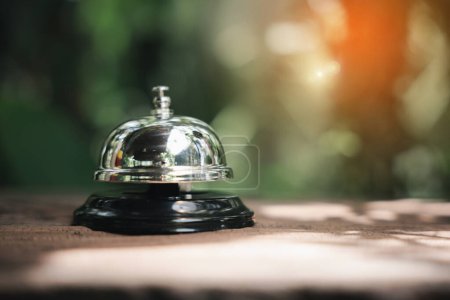 Photo for Hotel ring bell. Vintage bell to call staff outdoor in garden with green leaf, Closeup of silver service restaurant bell on wooden counter desk - Royalty Free Image