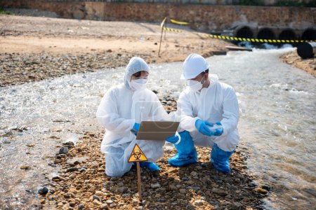 Photo for Biologist wear protective suit and mask collects sample of waste water from industry, problem environment, Ecologist sample taken dead fish to inspection and save data to laptop computer, Toxic water - Royalty Free Image