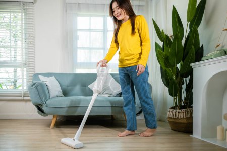 Photo for Housewife female dust cleaning floor under sofa or couch furniture with vacuum cleaner, Happy Asian young woman with accumulator vacuum cleaner at home in living room, household and housework concept - Royalty Free Image