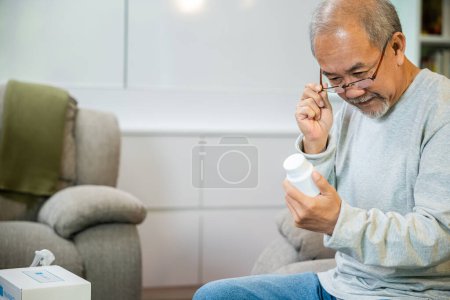 Foto de Asiático preocupado hombre mayor con píldoras medicinales para tomar en la mesa en la sala de estar, anciano comprar hierbas auto cura píldora Rx en línea de la farmacia, aislamiento en el hogar, servicio de ayuda de atención médica - Imagen libre de derechos