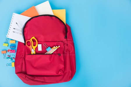 Téléchargez les photos : Pose plate de sac d'école rouge avec vue sur le dessus sac à dos et accessoires outils pour l'éducation des enfants sur fond bleu, concept de retour à l'école et espace de copie pour une utilisation - en image libre de droit