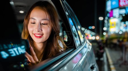 Téléchargez les photos : Happy beautiful woman texting smartphone sitting back seat her car in urban, Asian businesswoman commuting from office in Taxi backseat with mobile phone on road in city at night after late work - en image libre de droit