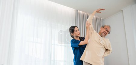 Foto de Rehabilitation of disabled people. Old senior man enjoys training with physiotherapist for outstretched arms at home, Asian physical therapist patient help elderly exercising arm stretch - Imagen libre de derechos