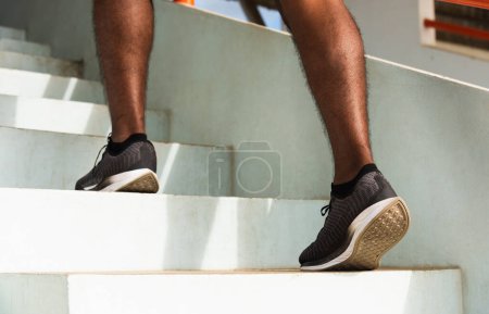 Téléchargez les photos : Gros plan chaussures d'athlète de jambes jeune coureur de sport homme noir étape en cours d'exécution jusqu'à monter des escaliers faire de l'entraînement cardio sport séance d'entraînement à la rue en plein air, exercice sain avant concept d'entraînement - en image libre de droit