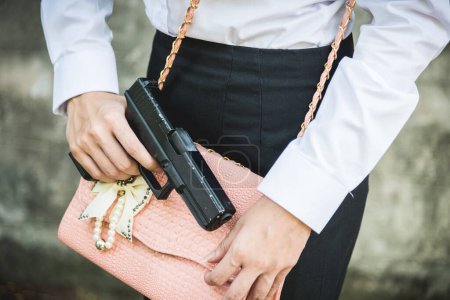 Photo for Young woman self defence putting gun in her small handbag, female hide gun in his chest, self-defense criminal concept - Royalty Free Image