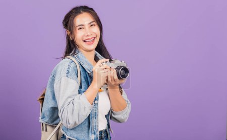 Photo for Attractive portrait happy Asian beautiful young woman smiling excited wear denims and bag holding vintage photo camera, female traveler female photographer, studio shot isolated on purple background - Royalty Free Image