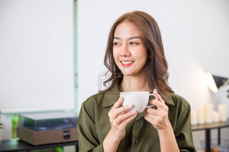Foto de Portrait of Happy beautiful woman rest in summer after wakeup at office room, Asian young woman hands holding hot coffee or tea cup for drink in morning while posing, white porcelain mug mock up - Imagen libre de derechos