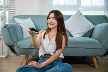 Photo for Asian young woman smiling sitting relax watch TV holding remote control on sofa in living room, Happy female fun movie holding remote watching television, Activity lifestyles concept - Royalty Free Image