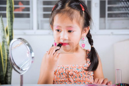 Photo for Happy kid is beautiful make up with cosmetics toy, Asian adorable funny little girl making makeup her face she looking in the mirror and applying red lipstick to mouth, Learning activity to be woman - Royalty Free Image