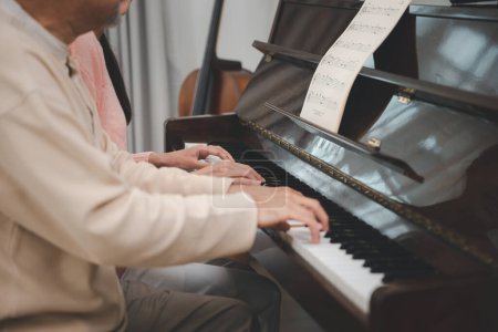 Photo for Family care. Happy daughter and elderly father playing music on the piano together in living room, Asian young woman teaching piano for senior man teaching at home, lifestyle life after retirement - Royalty Free Image