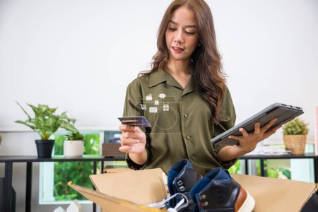 Photo for Asian young woman received online shopping parcel opening boxes to checking on digital tablet, woman holding credit card, happy female unpacking cardboard box, Shop online and delivery concept - Royalty Free Image