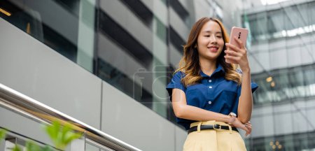 Photo for Young woman walking in the city with blue shirt and using smartphone. Girl using smart phone app for messaging, browsing and shopping. - Royalty Free Image