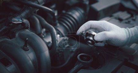 Photo for Skilled mechanic examining engine with dipstick in car workshop. Horizontal photo of male technician rubbing chin in deep thought. Concept for car maintenance and service. - Royalty Free Image