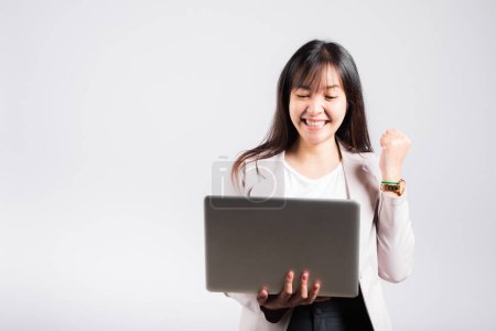 Foto de Mujer sonriendo confiado sosteniendo el uso de ordenador portátil y emocionado celebrando el éxito, Retrato emocionado feliz Asiática joven mujer decir sí a ganar estudio tiro aislado sobre fondo blanco - Imagen libre de derechos
