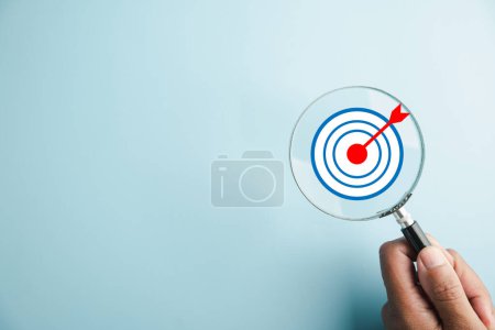 Photo for The magnifier glass centers on a target board, showcasing the importance of business objectives, it signifies the concepts of search, goal setting, strategy, and achieving success. - Royalty Free Image