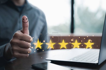Photo for Satisfied customer concept. Hand holding up a thumb with a smiley face and five-star rating symbol in background. Perfect for reviews, surveys, feedback in business and marketing. Copy space available - Royalty Free Image