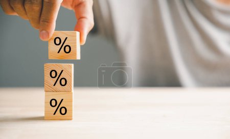 Photo for Concept of interest rate and financial rates. Hand placing a wooden cube block on top, symbolizing an increasing trend, with an upward direction icon and percentage symbol. - Royalty Free Image
