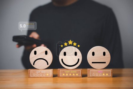 Photo for Mans hand selects the best smiley face on a wooden block circle to rate excellent business services and customer experience. Satisfaction survey concept. - Royalty Free Image