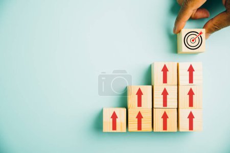 Photo for Target icon placed on wooden blocks, accompanied by upward arrows. Bar graph chart steps symbolize business growth on blue background, emphasizing profit, investment, and economic improvement concepts - Royalty Free Image