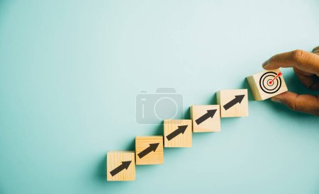 Photo for Wooden blocks with a prominent Target icon and rise up arrows. Bar graph chart steps illustrate business growth on a blue background. Represents profit, investment, and economic improvement concepts. - Royalty Free Image