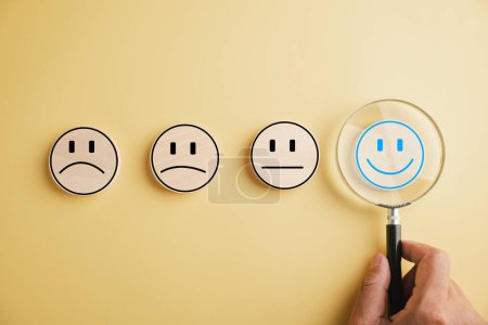 Photo for Magnifier in hand focuses on happy smiley face icon among emotions. Good feedback rating and positive customer review. Experience, satisfaction survey. Certificate symbolizes satisfaction. - Royalty Free Image