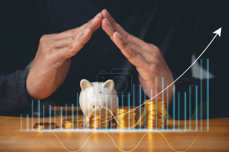 Photo for Piggy bank investment - businessman hand placing coins in a piggy bank with a graph of investment returns in the background. Concept for financial security and savings. - Royalty Free Image