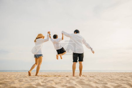 Photo for Family outdoor activities, Back family mother, father and son holding hands and jumping in air at dawn time, Happy Asian family people have fun together on beach on holiday summer vacation travel - Royalty Free Image