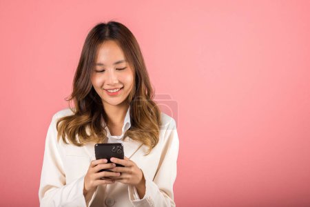 Foto de Feliz asiática retrato hermosa linda joven mujer adolescente sonriente emocionado mantenga inteligente teléfono móvil estudio disparo aislado en rosa fondo, Mujer sorprendida y sms chat en línea en el teléfono inteligente - Imagen libre de derechos