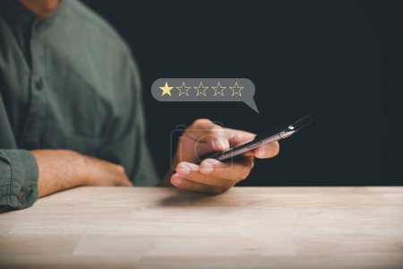 Photo for Unhappy client uses smartphone to give a 1-star satisfaction rating on social media. Negative feedback concept impacting business reputation and customer perception. - Royalty Free Image