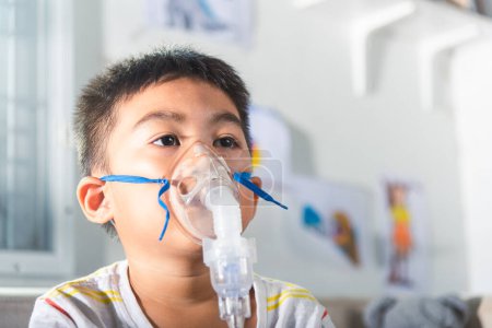 Photo for Asian Child using nebulizer mask equipment alone have smoke, Kid boy making makes inhalation nebulizer steam sick cough at home, oxygen spray inhaler therapy, stuffy nose and runny, Health medical - Royalty Free Image