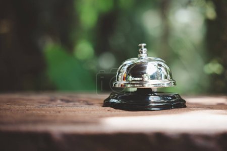 Photo for Hotel ring bell. Closeup of silver service restaurant bell on wooden counter desk, vintage bell to call staff outdoor in garden with green leaf - Royalty Free Image