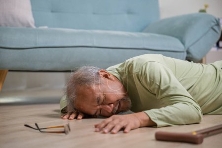 Foto de Anciano cayendo en el suelo solo con bastón en la sala de estar en casa, Hombre mayor dolor de cabeza acostado en el suelo después de caer, Cuidado de la salud y el concepto de medicina - Imagen libre de derechos