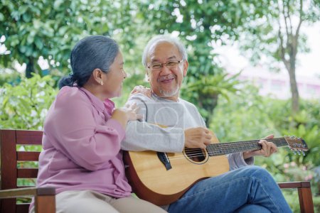 Téléchargez les photos : Heureux asiatique couple âgé homme âgé jouer de la guitare tandis que sa femme chanter ensemble à l'extérieur à la maison, Activité soins de santé familiale, Profiter du mode de vie pendant la vie de retraite en s'amusant de personnes âgées - en image libre de droit