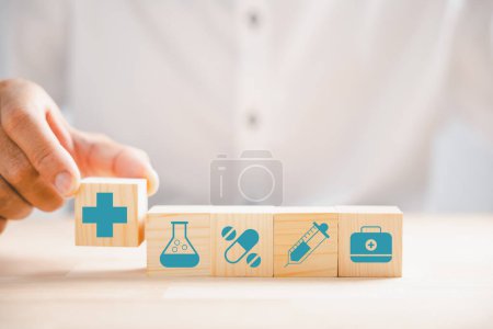 Photo for Captured moment, Hand clutches wooden block with healthcare and medical icons. Portrays safety, health, and family well-being, symbolizing pharmacy, heart care, and happiness. health care concept - Royalty Free Image