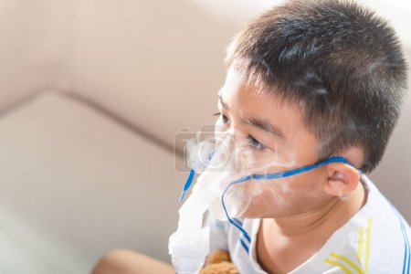 Photo for Asian Child using nebulizer mask equipment alone have smoke, Kid boy making makes inhalation nebulizer steam sick cough at home, oxygen spray inhaler therapy, stuffy nose and runny, Health medical - Royalty Free Image
