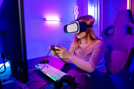 Photo for Gamer in VR headset glasses exploring metaverse play video game online with joystick on computer neon lights, Excited woman virtual playing gamepad controller she very determined at home - Royalty Free Image