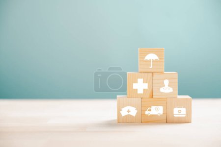 Téléchargez les photos : Cubes en bois en forme de pyramide, métaphore de la santé et de l'assurance. En plus, une icône d'assurance médicale transmet la sécurité. Fond bleu avec copyspace pour le message d'assurance maladie. - en image libre de droit