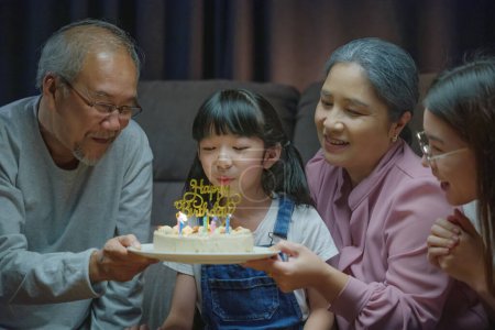 Foto de Sorpresa de cumpleaños. Feliz familia asiática abuelos y madre celebrando disfrutar de fiesta de cumpleaños con pastel de nieta en casa en la noche - Imagen libre de derechos