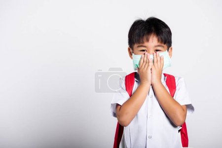 Photo for Asian student kid boy wearing student thai uniform and medical protect face mask and hand cover mouth in studio shot isolated on white background, new normal back to school - Royalty Free Image