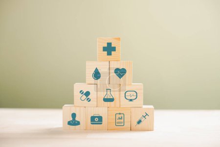 Foto de Concepto de salud y seguro representado a través de una pirámide de cubos de madera. Coronado con un icono de seguro médico sobre un fondo blanco, creando espacio para el mensaje de Seguro de Salud. - Imagen libre de derechos