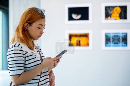 Photo for Visitor woman standing takes picture art gallery collection in front framed paintings pictures on white wall with mobile phone, people watch at photo frame with smartphone at artwork gallery show - Royalty Free Image