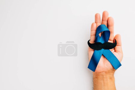 Téléchargez les photos : Soutenir la santé des hommes et la sensibilisation au cancer de la prostate en novembre. Mans mains tiennent un ruban bleu clair avec une moustache sur un fond bleu un symbole de force et de solidarité. - en image libre de droit