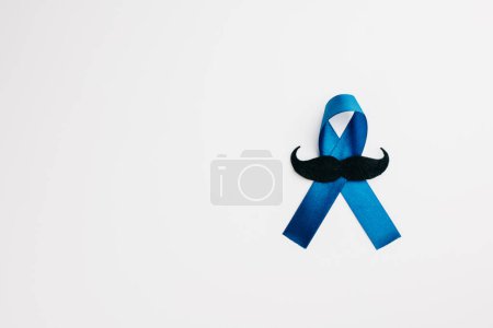 Téléchargez les photos : Un ruban bleu avec une moustache, symbolisant le soutien à la santé des hommes, repose sur un fond blanc. Idéal pour la santé, la Journée internationale des hommes et les concepts de la Journée des pères. - en image libre de droit