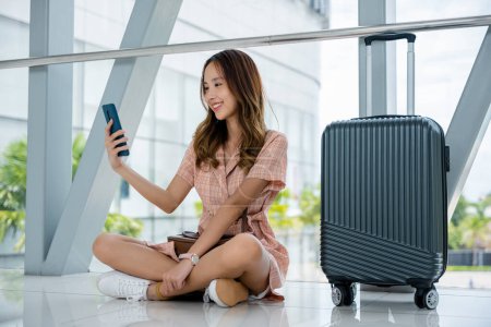 Téléchargez les photos : Femme heureuse souriant et textant sur son smartphone en attendant son vol à l'aéroport. Voyage touristique concept de voyage - en image libre de droit
