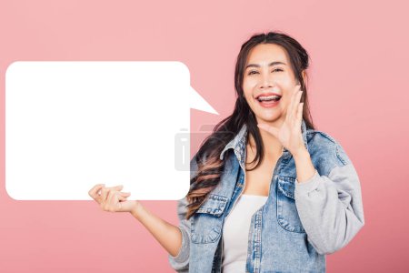 Photo for Happy Asian beautiful young woman smiling excited wear denims hand near mouth announce news and holding empty speech bubble sign, Portrait female posing idea, studio shot isolated on pink background - Royalty Free Image