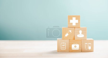 Photo for Healthcare and insurance visualized by a pyramid arrangement of wooden cubes. Crowning medical icons symbolize safety. Blue background offers copyspace to articulate Health Insurance concepts. - Royalty Free Image